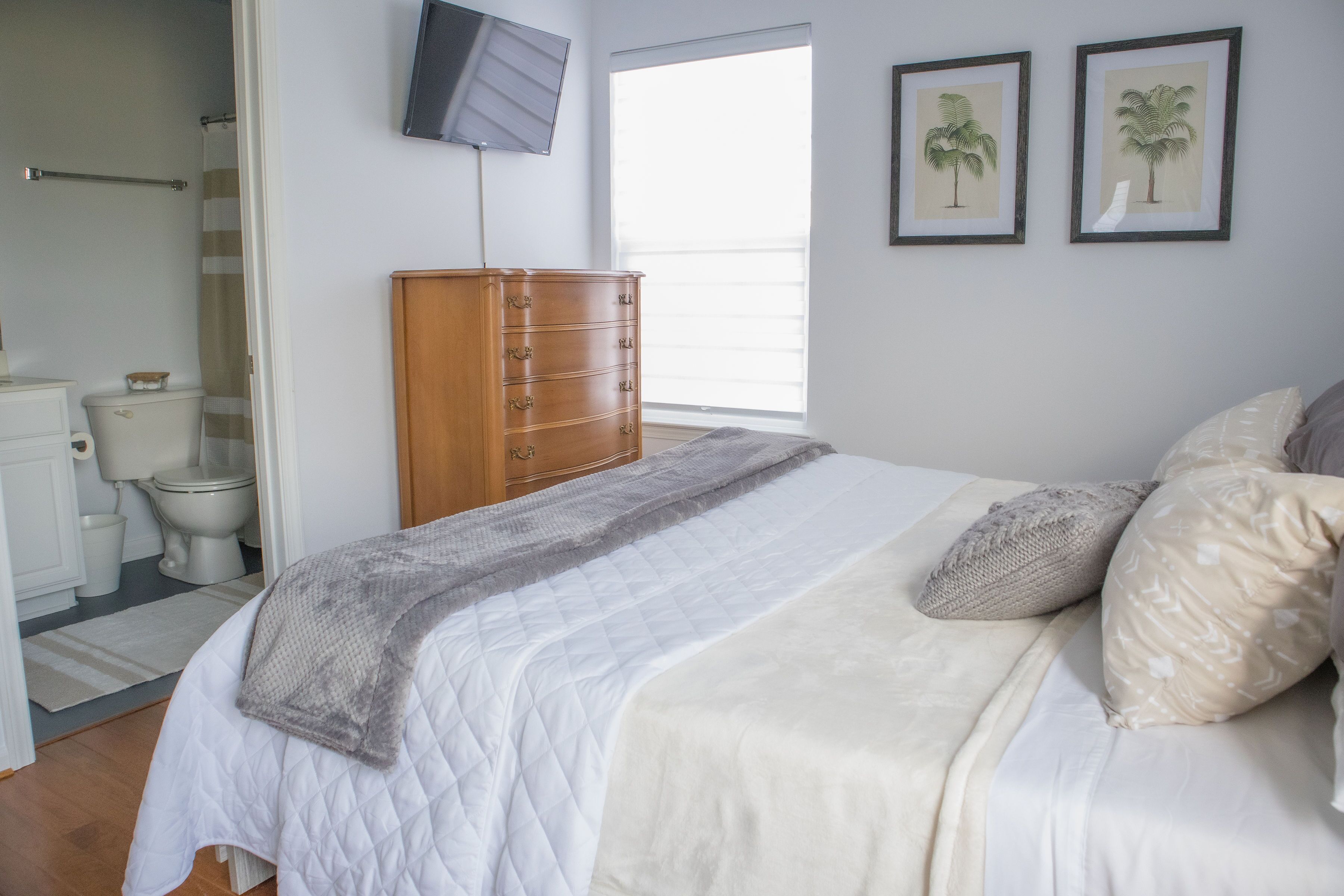 A bedroom with a bed, a dresser, a television, and two framed pictures on the wall.