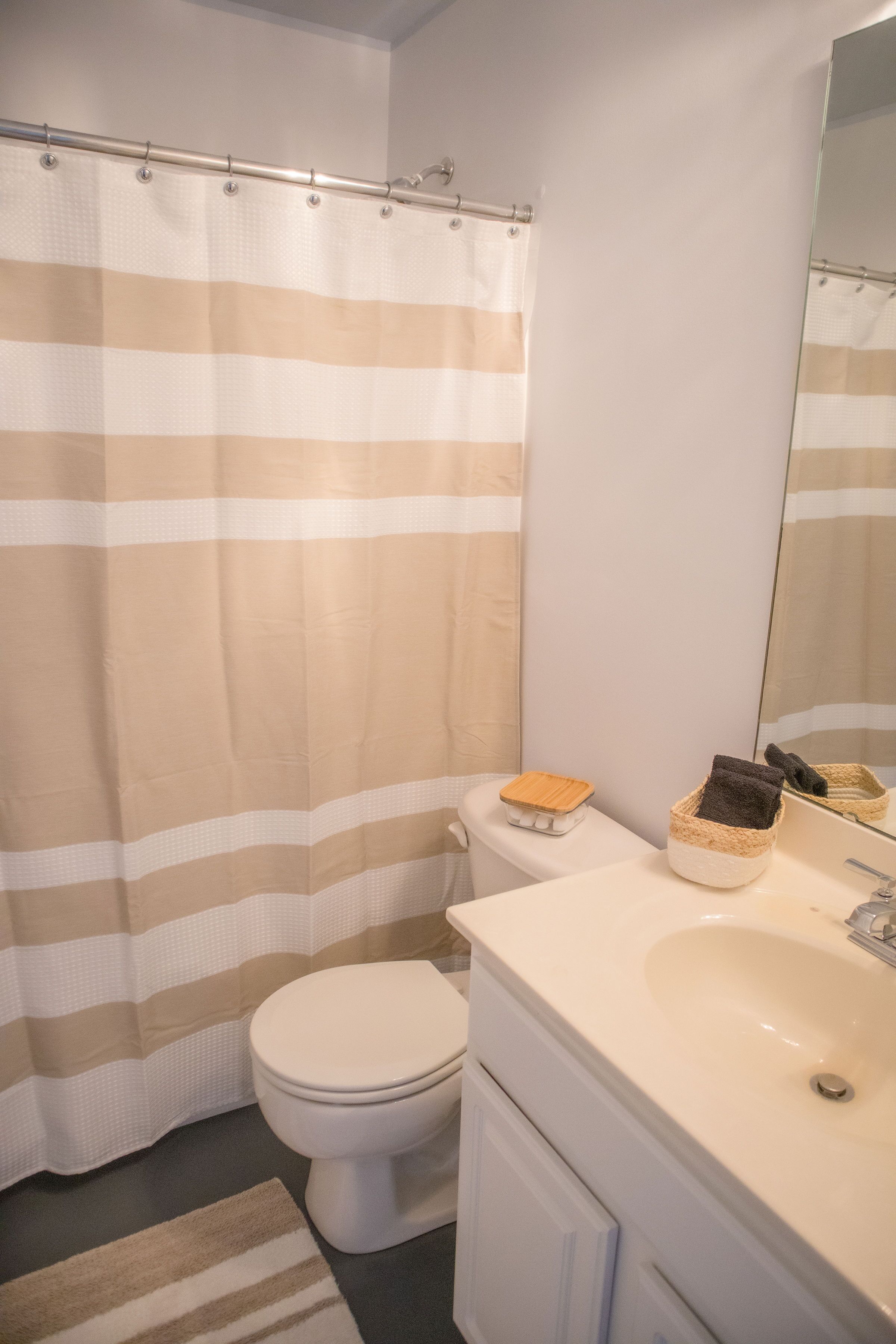 Une salle de bain avec un rideau de douche à rayures, des toilettes, un lavabo avec un miroir et un petit tapis.