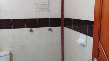 Un baño pequeño con azulejos, ducha, inodoro y puerta de madera.