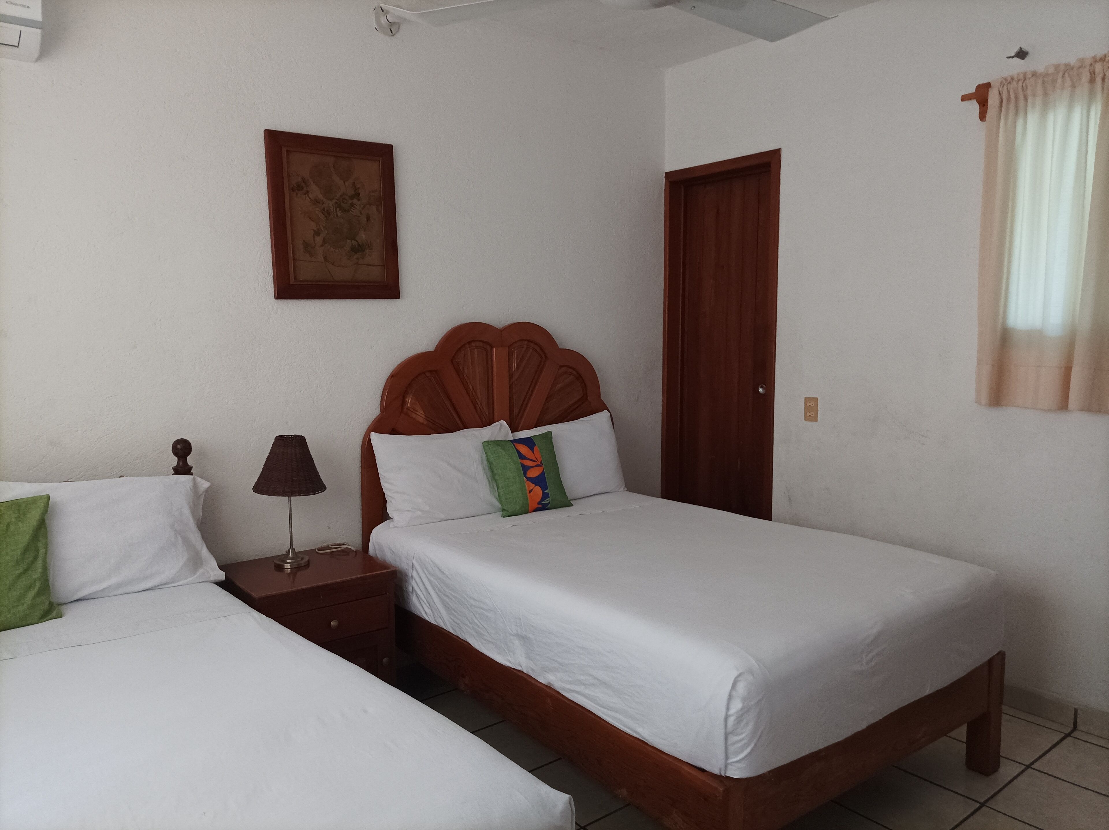 A bedroom with two single beds, a wooden headboard, a bedside table with a lamp, a door, and a wall-mounted picture.