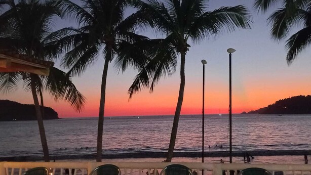 Une vue sur le coucher de soleil, avec des palmiers et une plage.