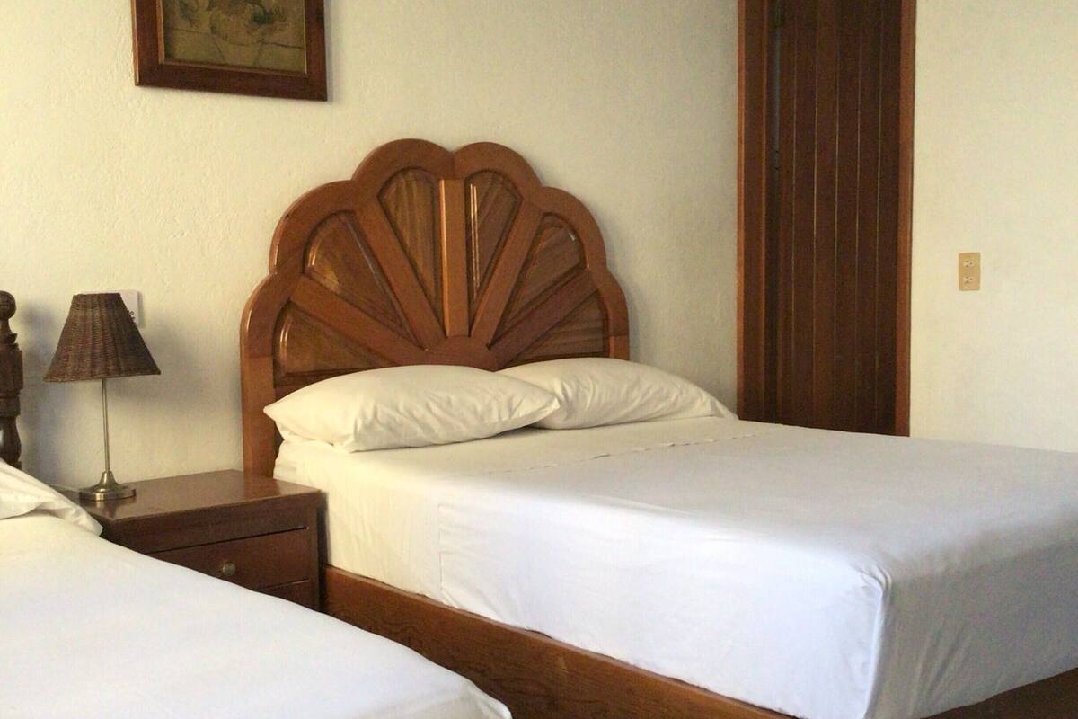 Une chambre avec deux lits simples, une tête de lit en bois, une table de chevet avec une lampe et une porte.