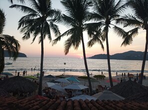 A beach with palm trees, umbrellas, and a sunset.