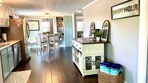 Une cuisine avec un plancher en bois, des armoires blanches, un coin repas avec des chaises et un espace dédié au café.