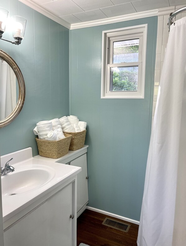 Une salle de bain avec un lavabo blanc, un miroir, une fenêtre et un rideau de douche.