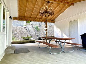 Eine Terrasse im Freien mit einem Holztisch und einer Bank, einer Chandelüster und einer Treppe, die in einen Garten führt.