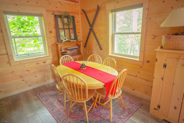 Ein Holzblockhaus-Interieur mit Esstisch, Stühlen, einer roten Bodenläufer und einem Schrank.