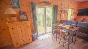 A cozy cabin interior with a wooden floor, a dining table with stools, a sofa, a television, and a bookshelf. - Smith Lake Cabin with Game Room (Marcell)