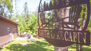 A sign for Smith Lake Cabin with a rustic design, surrounded by trees and a grassy yard. - Smith Lake Cabin with Game Room (Marcell)
