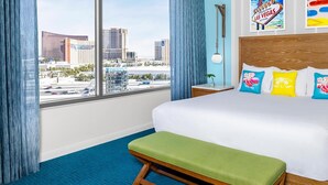 A hotel room with a large bed, a bench, a nightstand, a bedside table, and a view of the cityscape.