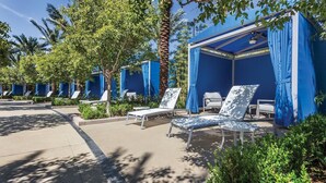A row of blue-roofed outdoor seating areas with sun loungers and umbrellas, surrounded by greenery and palm trees.