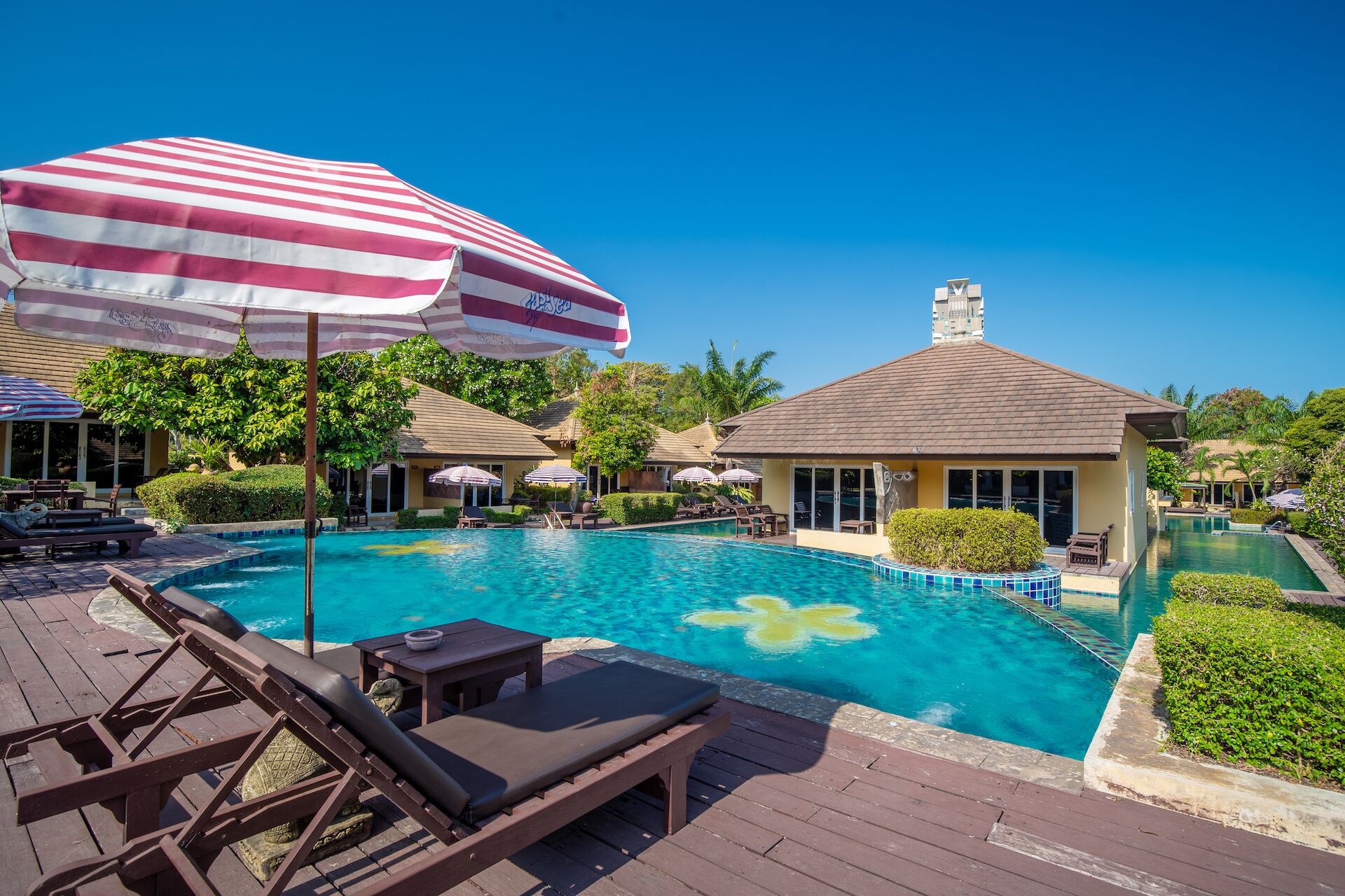 A pool area with lounge chairs and umbrellas, surrounded by buildings and greenery.