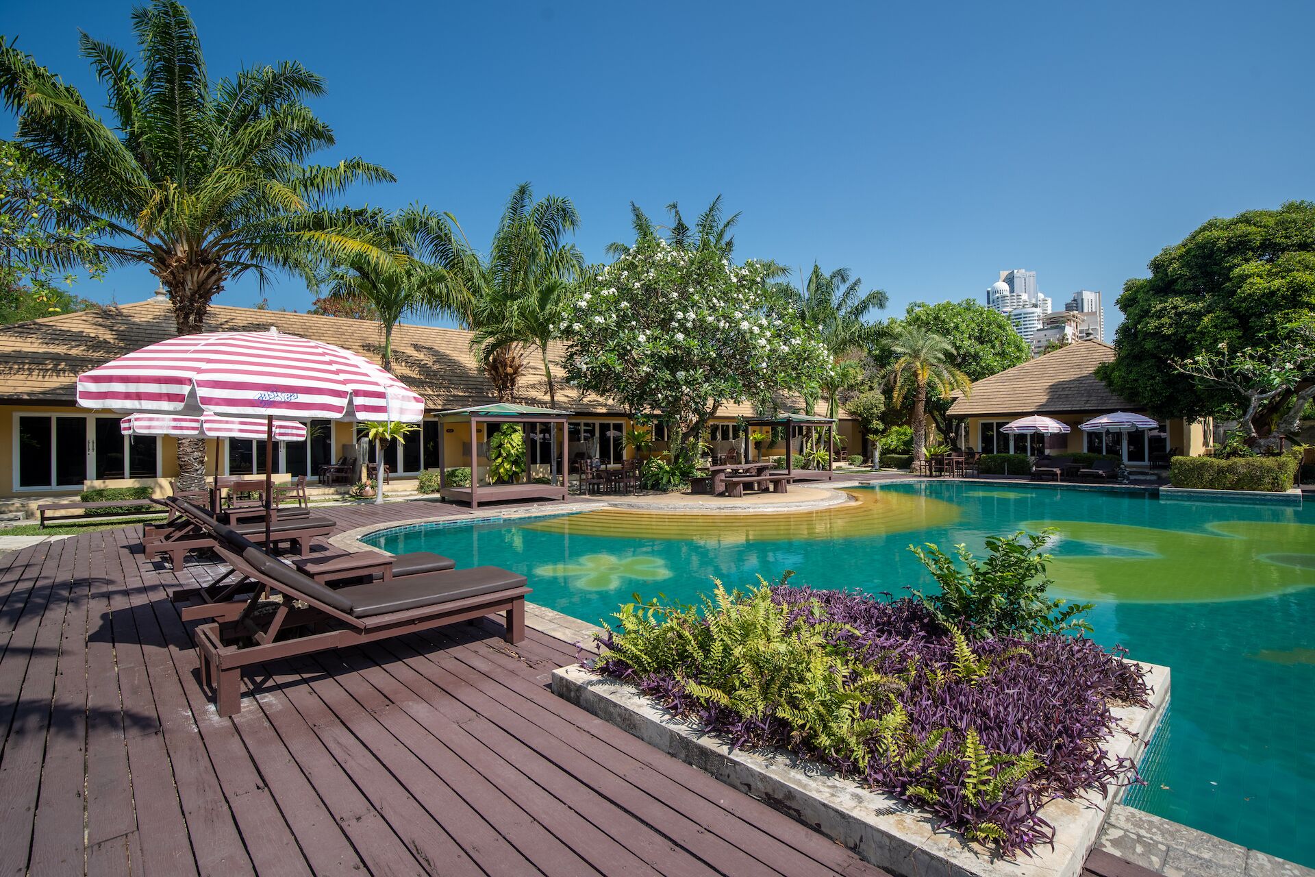 A resort pool area with lounge chairs, umbrellas, and a clear view of the city skyline.