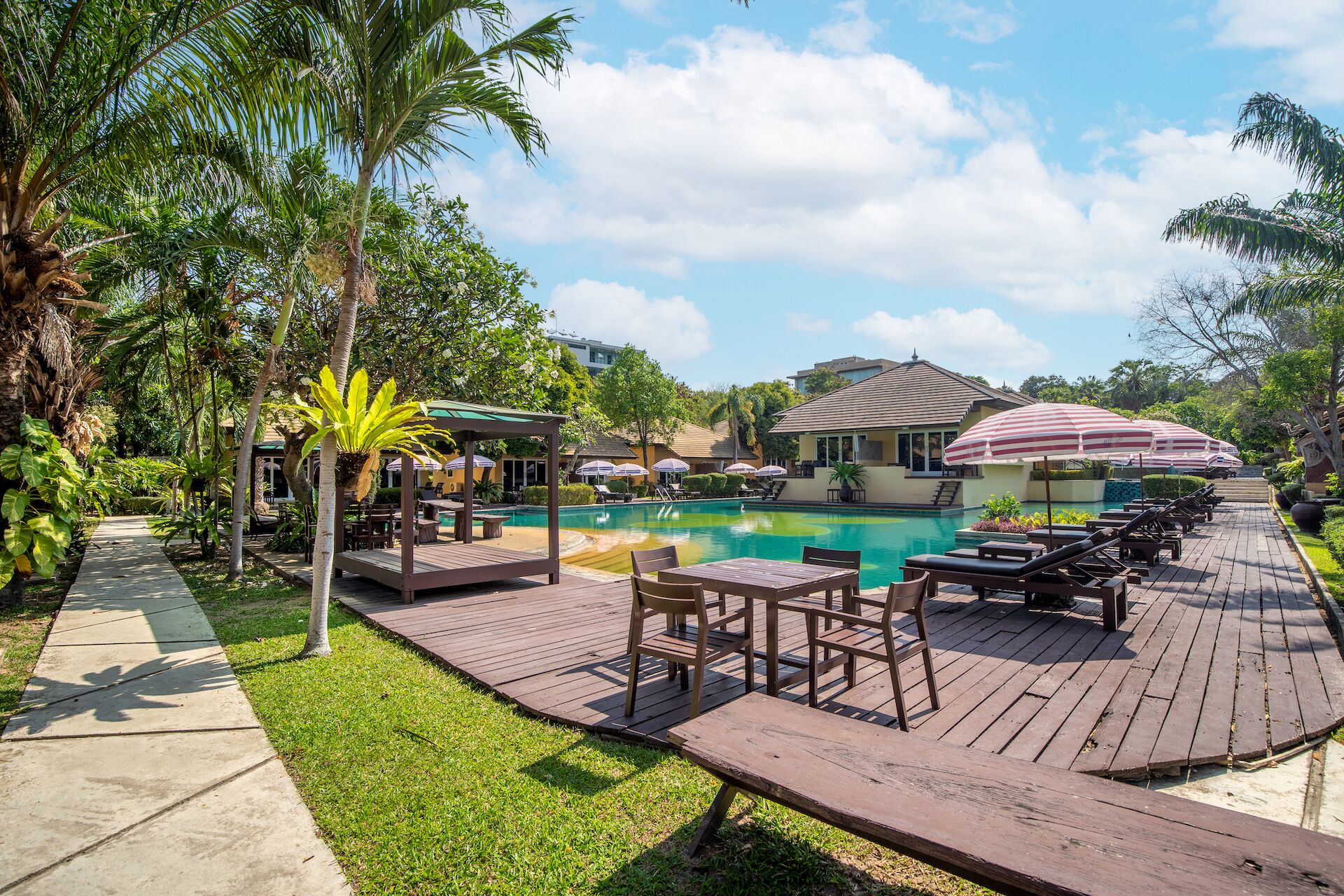 A poolside area with lounge chairs, a wooden deck, and a covered seating area.