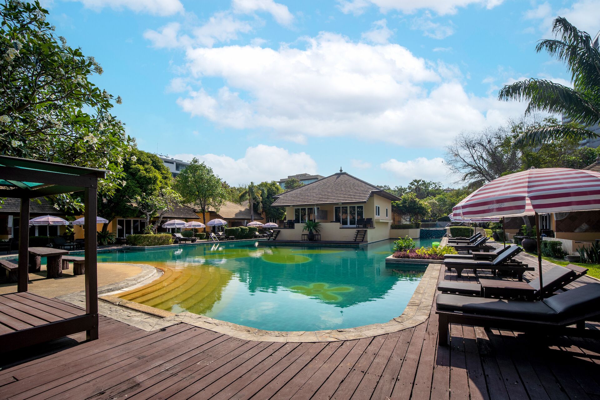 A pool area with lounge chairs, umbrellas, and a gazebo.