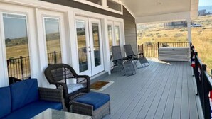 Ein überdachter Außenbereich mit Holzterrasse, zwei Korbstühle mit Kissen, einem blauen Sofa und einem Geländer.