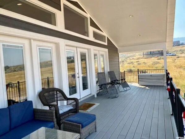 Un espace extérieur abrité doté d’une terrasse en bois, de deux fauteuils en osier avec des coussins, d’un canapé bleu et d’une rambarde.