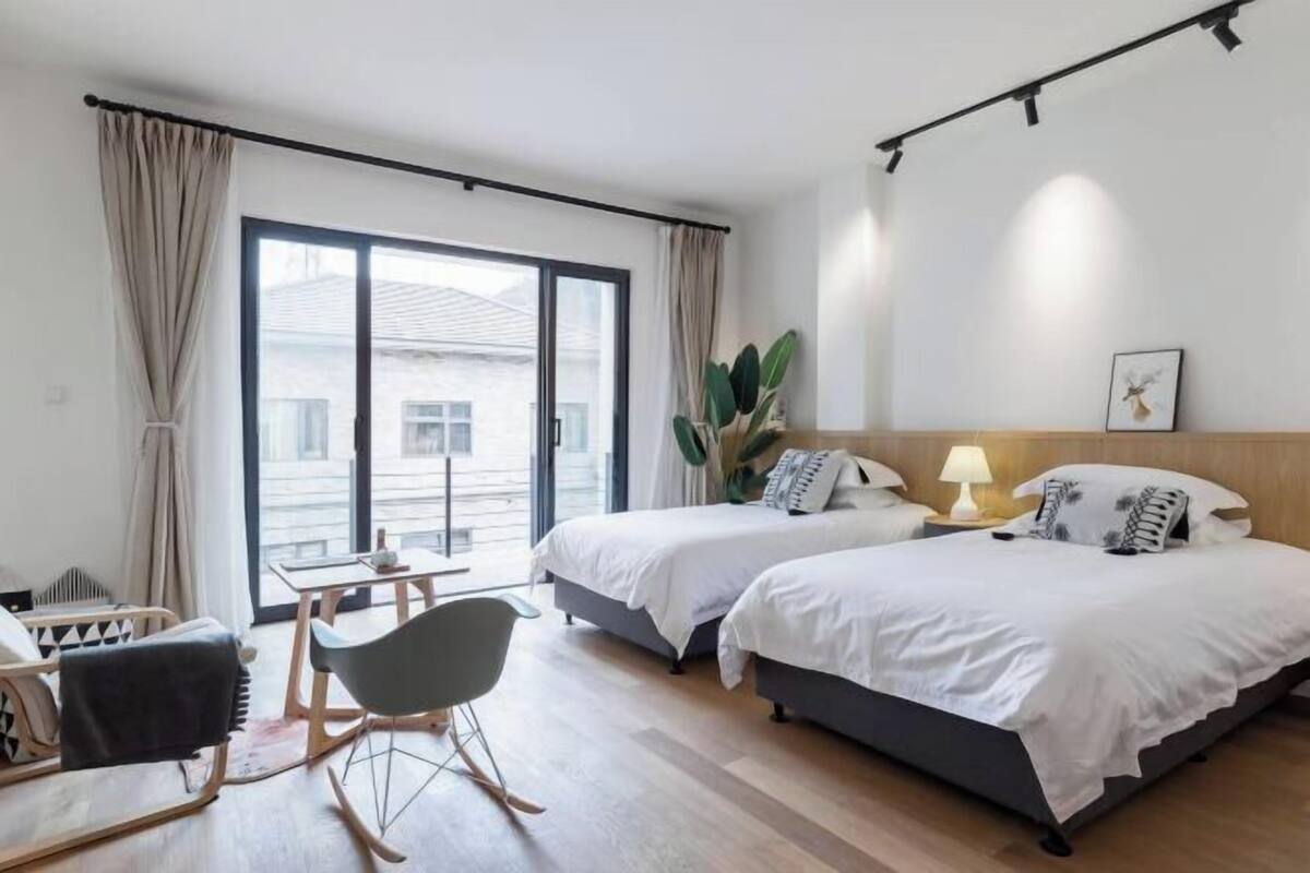 Una habitación de hotel con dos camas, un escritorio, una silla y un ventanal grande.