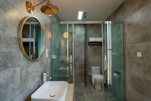 A modern bathroom with a glass-enclosed shower, a white sink, a round mirror, and a toilet. - Wonder Villa (Deqing)