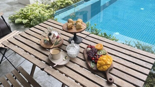 A wooden table with a breakfast setup including a cup, a glass, a plate with a spoon, a small cake, and a fruit platter with grapes, kiwi, and mango. - Wonder Villa (Deqing)