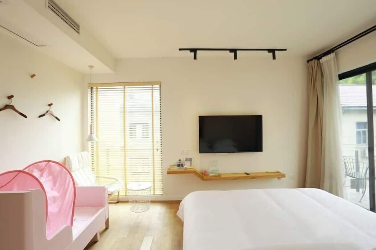 Habitación de hotel con una cama, televisor montado en la pared, una mesita y una ventana con persianas.