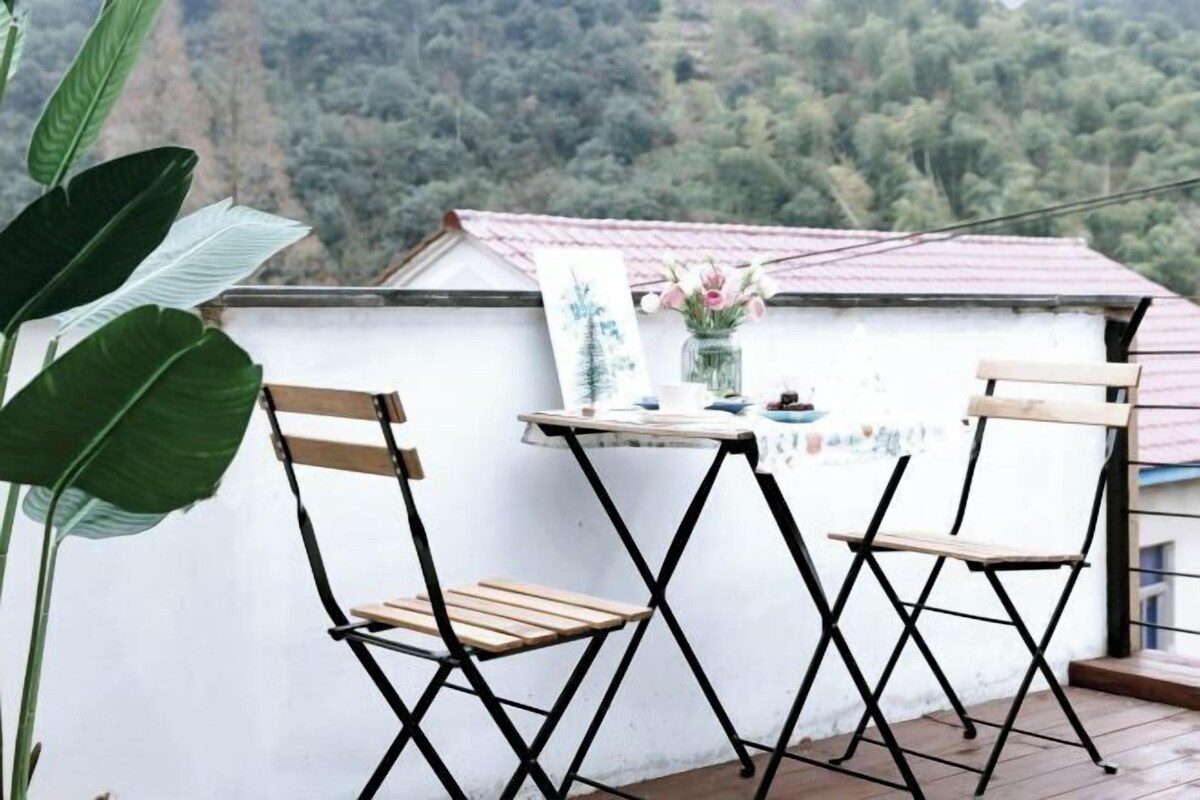 A small balcony with two wooden chairs, a table, and a vase with flowers.