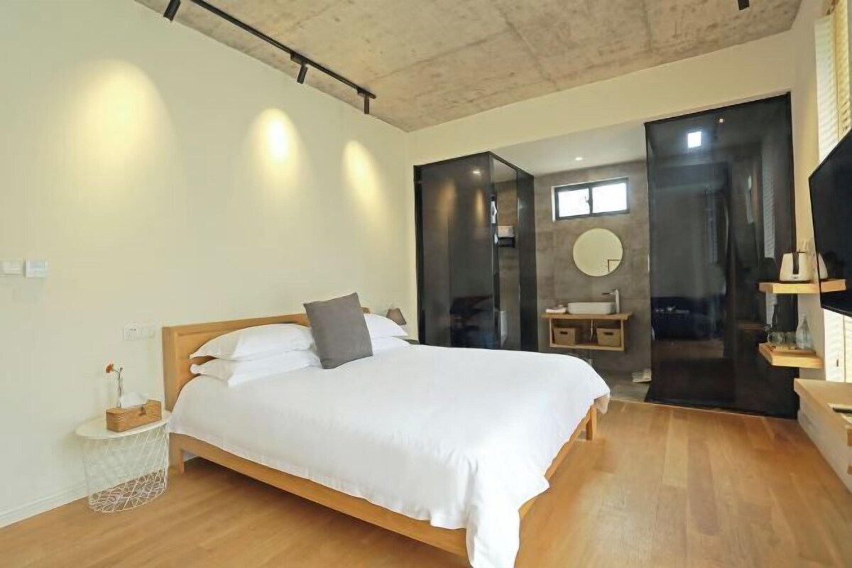 A modern bedroom with a wooden bed, a small bedside table, a round mirror, and a built-in sink.