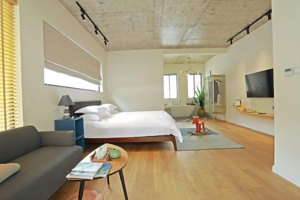 Una habitación de hotel moderna con cama, sofá y una pequeña mesa con objetos encima.