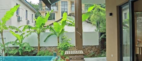 A poolside area with a wooden bench, a covered seating area, and a view of neighboring buildings.