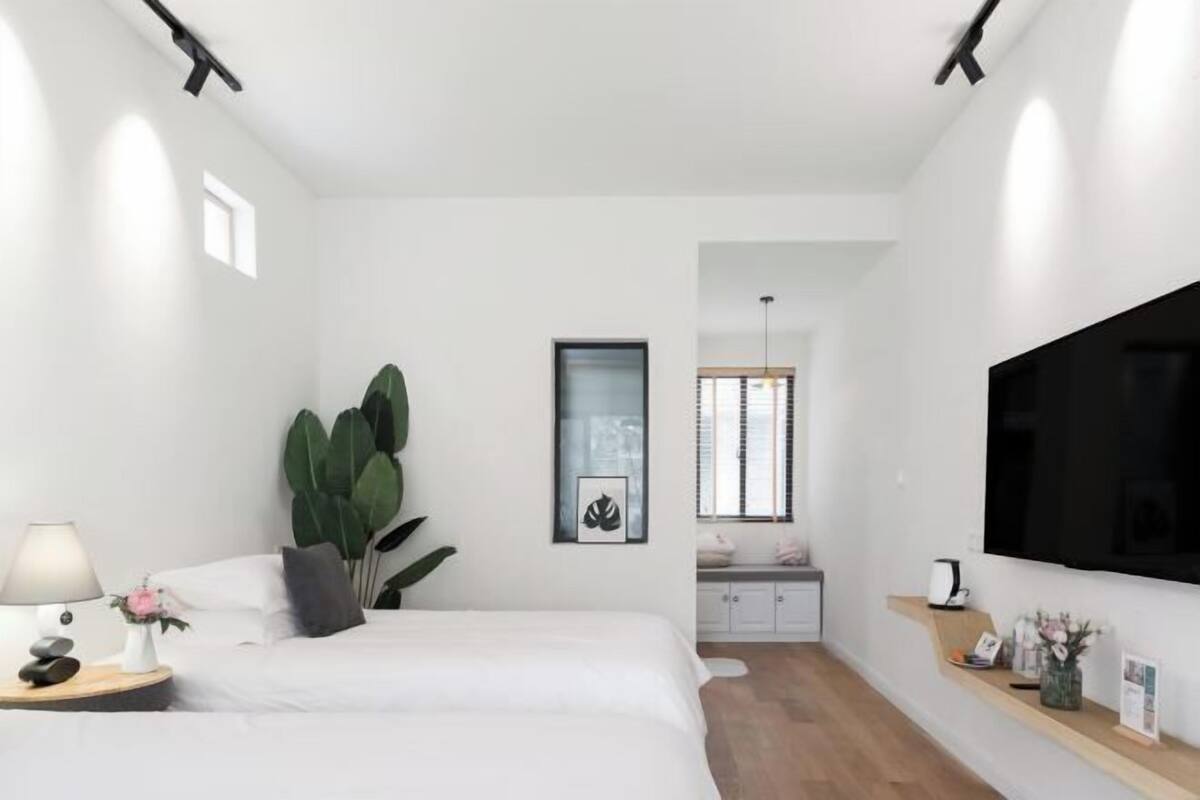 Un dormitorio moderno con cama, mesita de noche, lámpara y una planta grande.