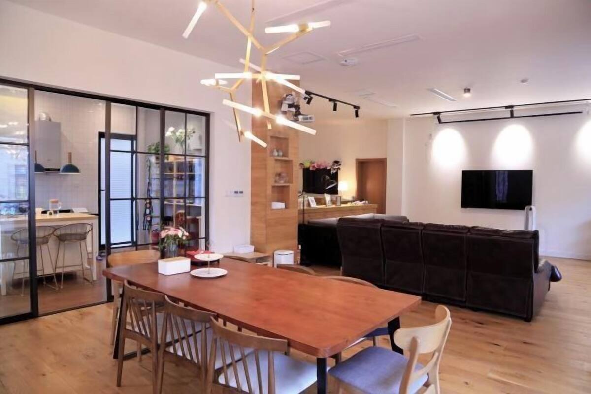 Un espacio de estar moderno con una mesa de comedor de madera, sillas, un sofá y un televisor montado en la pared.