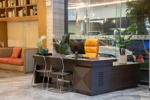 A reception desk with a computer, two chairs, a sofa, and a bookshelf. - Qianmen Holiday Inn (Zhuhai City Rail Mingzhu Station) (Zhuhai)
