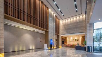 A spacious lobby with a polished marble floor, a reception area with a counter, and a large window offering a view of the outside.