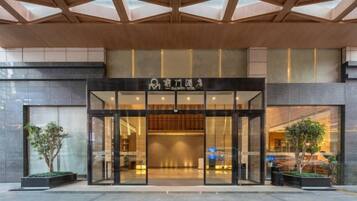 A hotel entrance with a modern design, featuring a glass facade and a wooden ceiling.