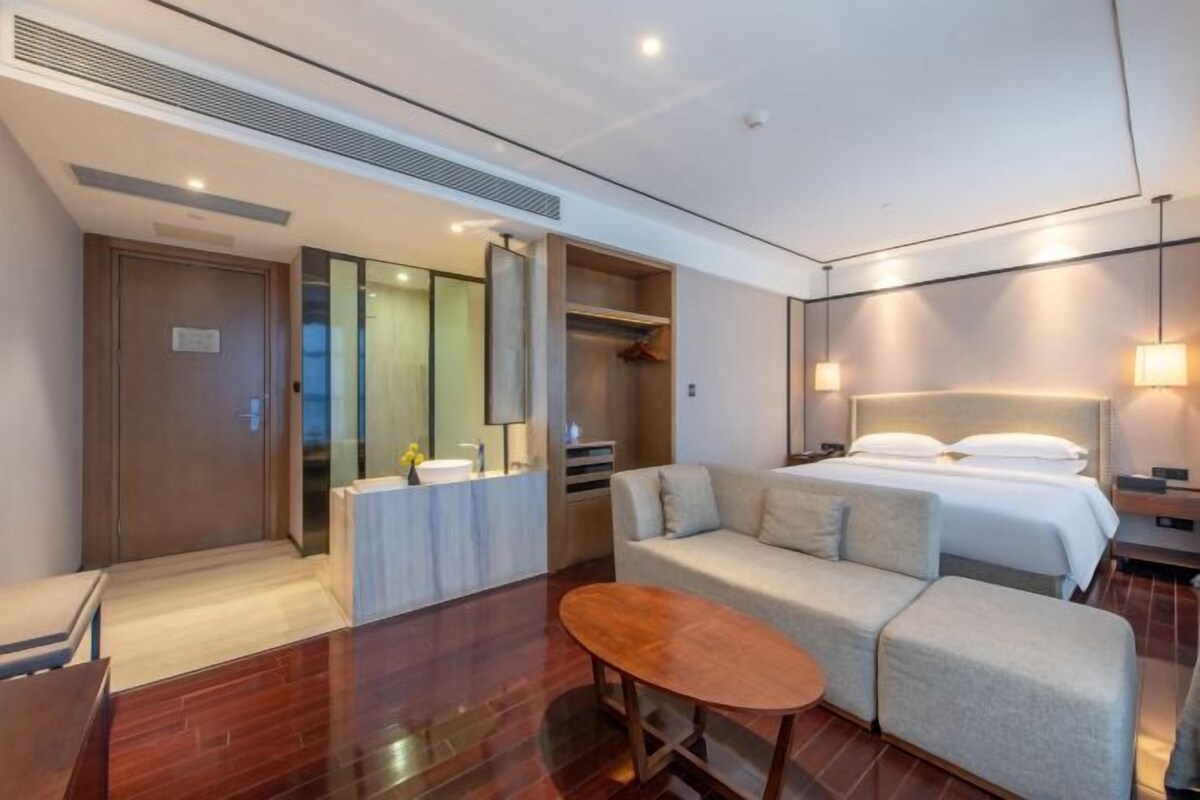 A hotel room with a bed, a sofa, a small table, a mirror, and a wardrobe.