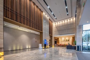 Un vestíbulo amplio con piso de mármol pulido, una recepción y un panel de madera grande a la izquierda.