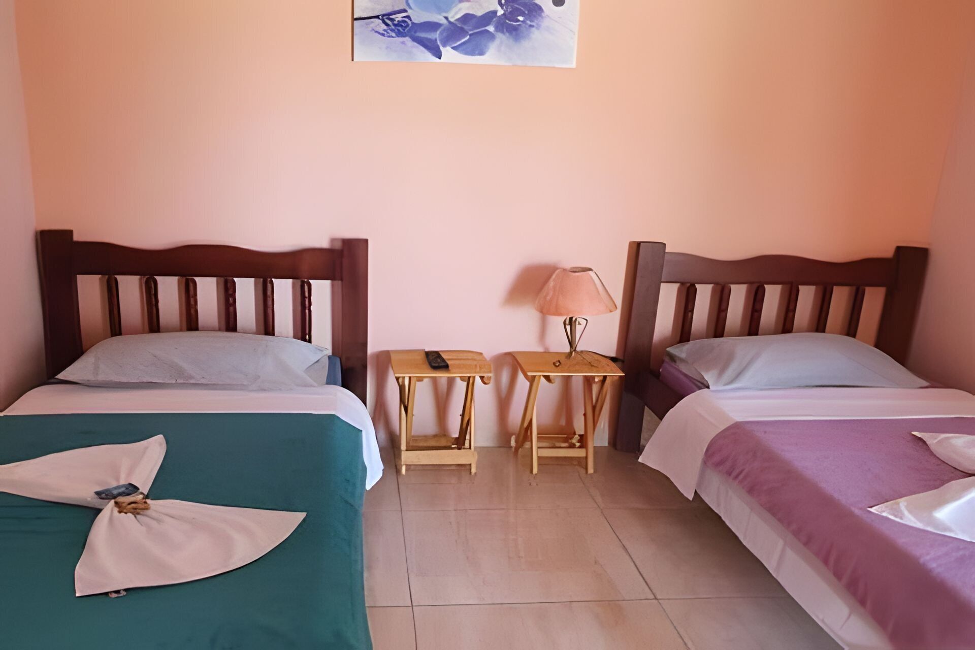 A room with two beds, each with a wooden headboard, a small table with a lamp, and a wall-mounted picture.