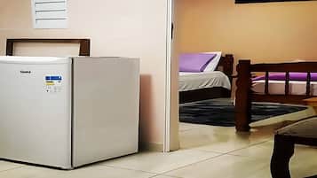 A compact room with a refrigerator, a bed with a purple pillow, and a wooden chair.