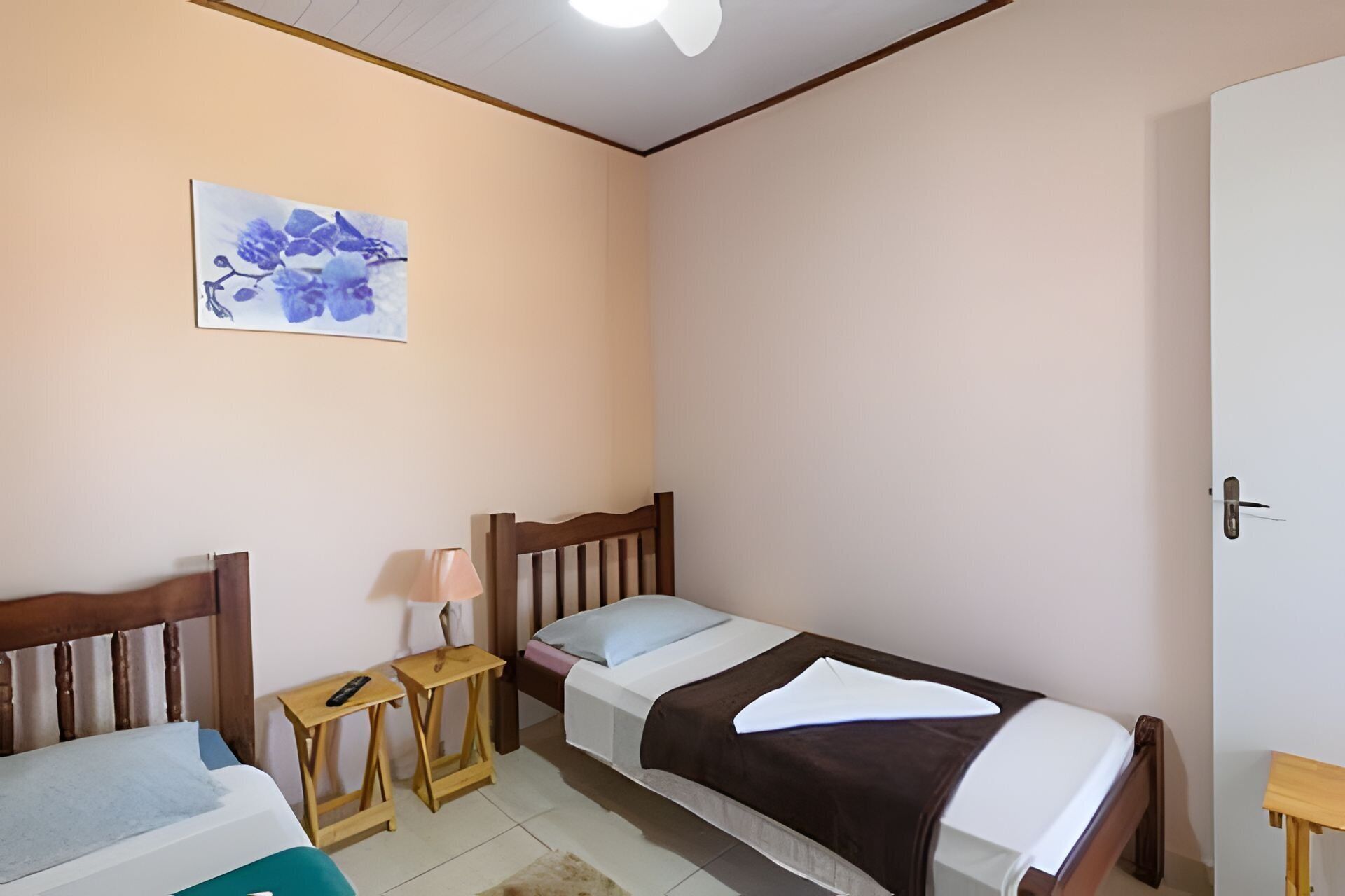 A small, simple room with two single beds, a bedside table with a lamp, and a wall-mounted artwork.