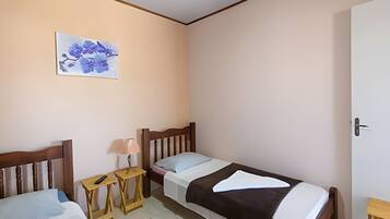 A small, simple room with two single beds, a bedside table with a lamp, and a wall-mounted artwork.