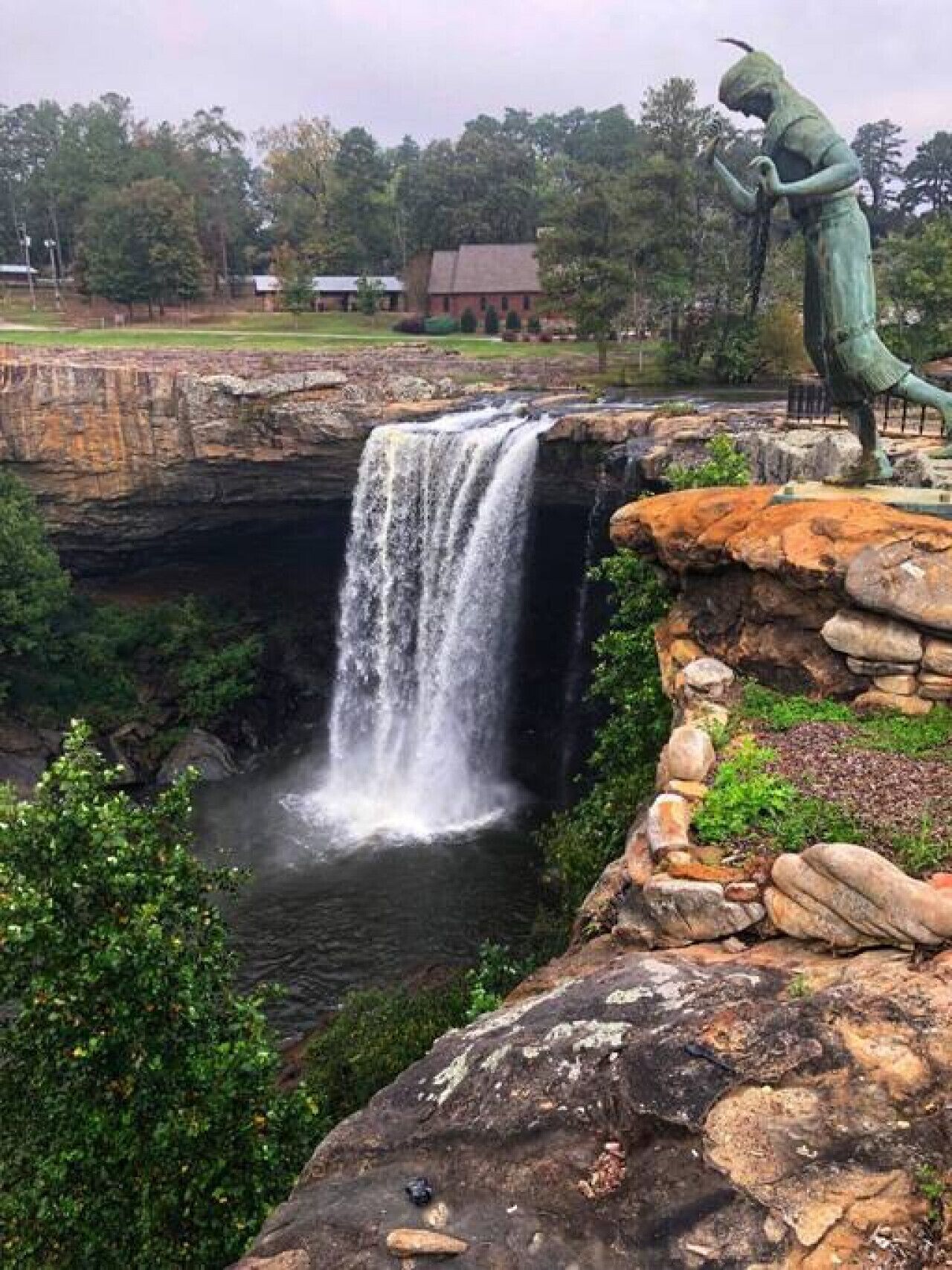 A waterfall cascading over a rocky ledge with a statue of a figure on the right.