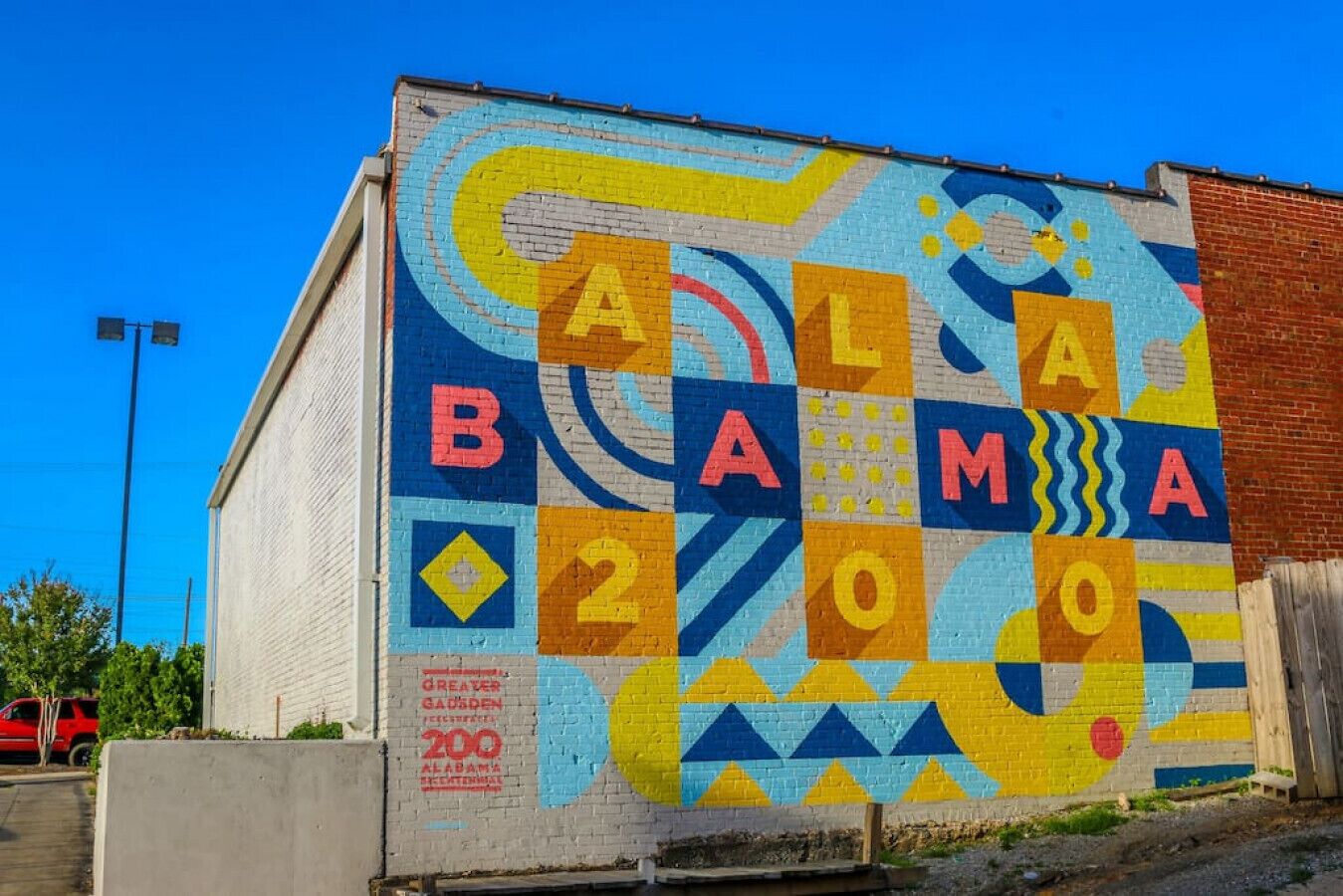 Une fresque colorée orne le mur d’un bâtiment, avec des motifs géométriques et les lettres « AALAMOO » bien visibles.