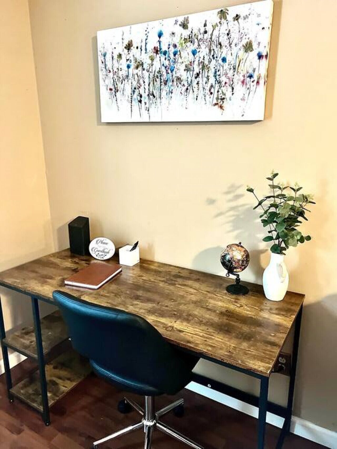 A wooden desk with a globe and a plant, a blue chair, and a framed artwork on the wall.