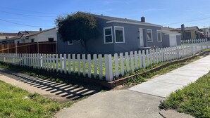 A residential house with a white picket fence, a tree in front, and a clear sky.