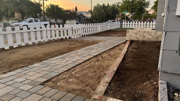 A paved pathway leading to a fenced area with a dirt section.
