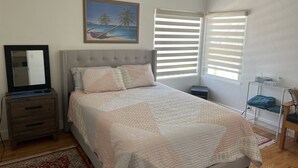 A bedroom with a bed, a dresser, a mirror, a painting, and a window with blinds.