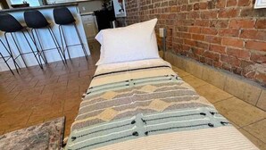 A bed with a patterned bedspread, a brick wall, and a kitchen area in the background. - The Loft On Broad - Gadsden’s First Downtown Loft (Gadsden)
