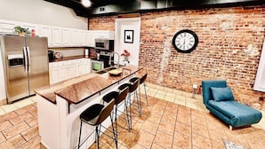 A modern kitchen with a brick wall, a clock, and a blue sofa. - The Loft On Broad - Gadsden’s First Downtown Loft (Gadsden)