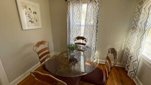 A dining area with a round glass table, four chairs, a potted plant, and patterned curtains. - *Hidden Gem Close 2 Everything * (Gadsden)