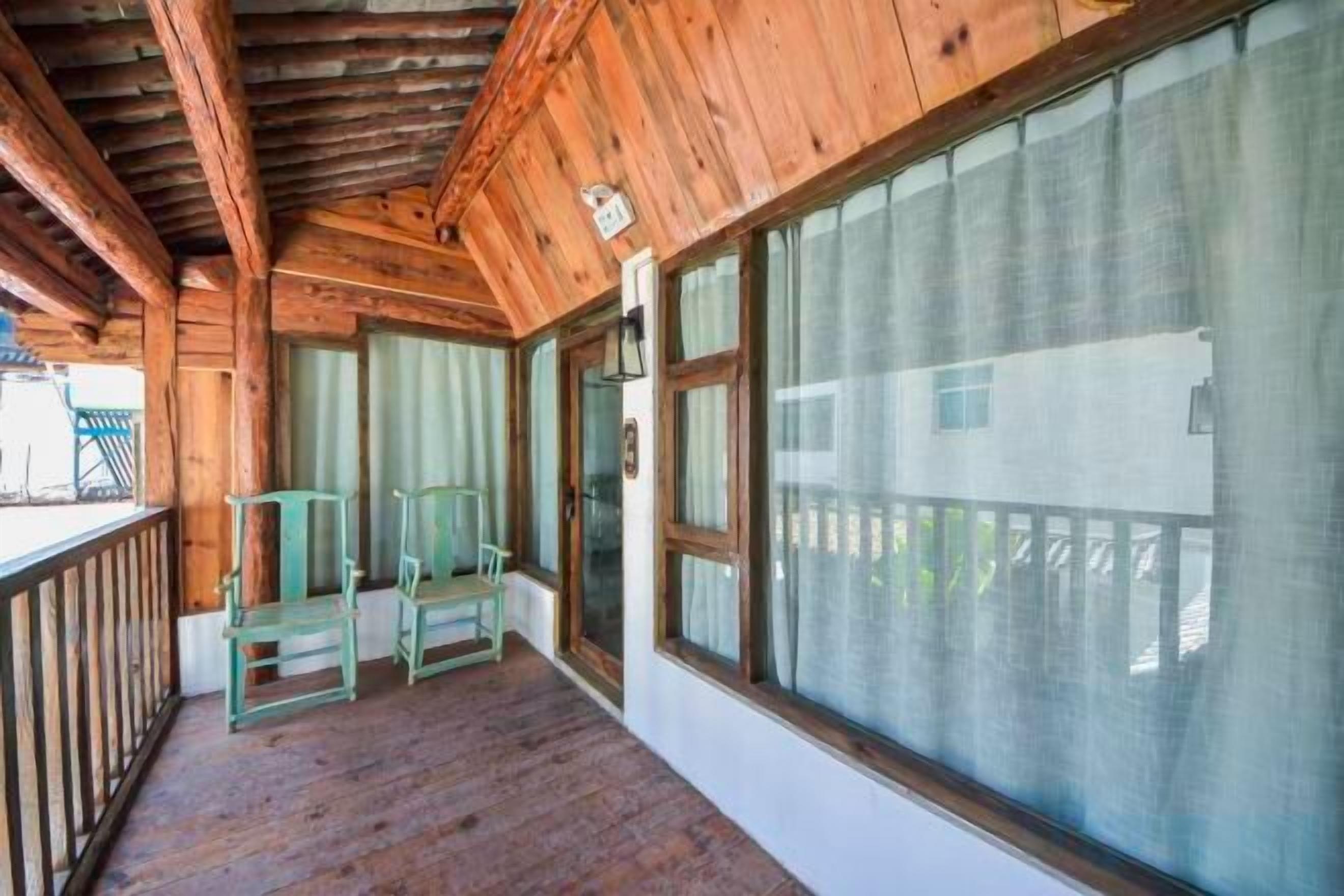 A wooden porch with a view of a building, two chairs, and a large window.